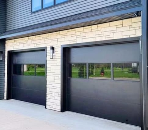 Two black garage doors with horizontal window lites on a stone and siding home